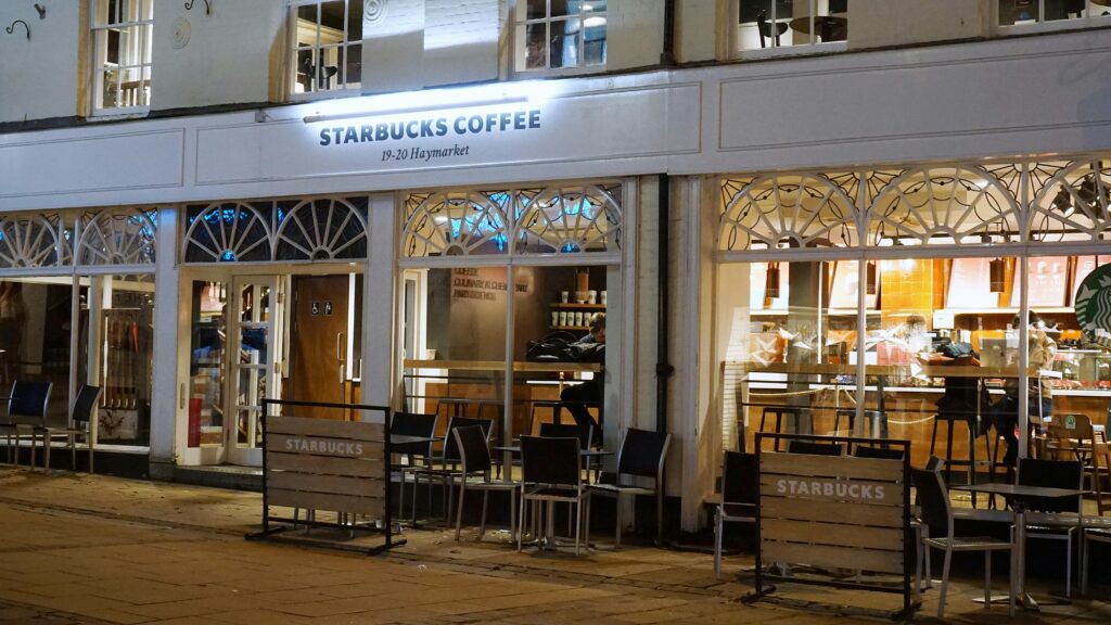 A cozy Starbucks café in Norwich with inviting exterior lights and seating at night.