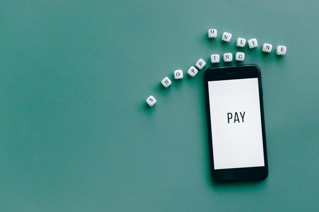 Image of smartphone displaying 'PAY' surrounded by dice spelling 'online shopping' on teal background.