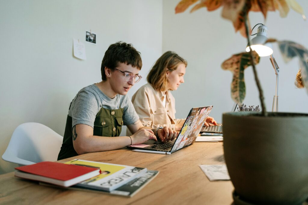 Two young professionals working collaboratively on laptops in a modern and creative workspace.