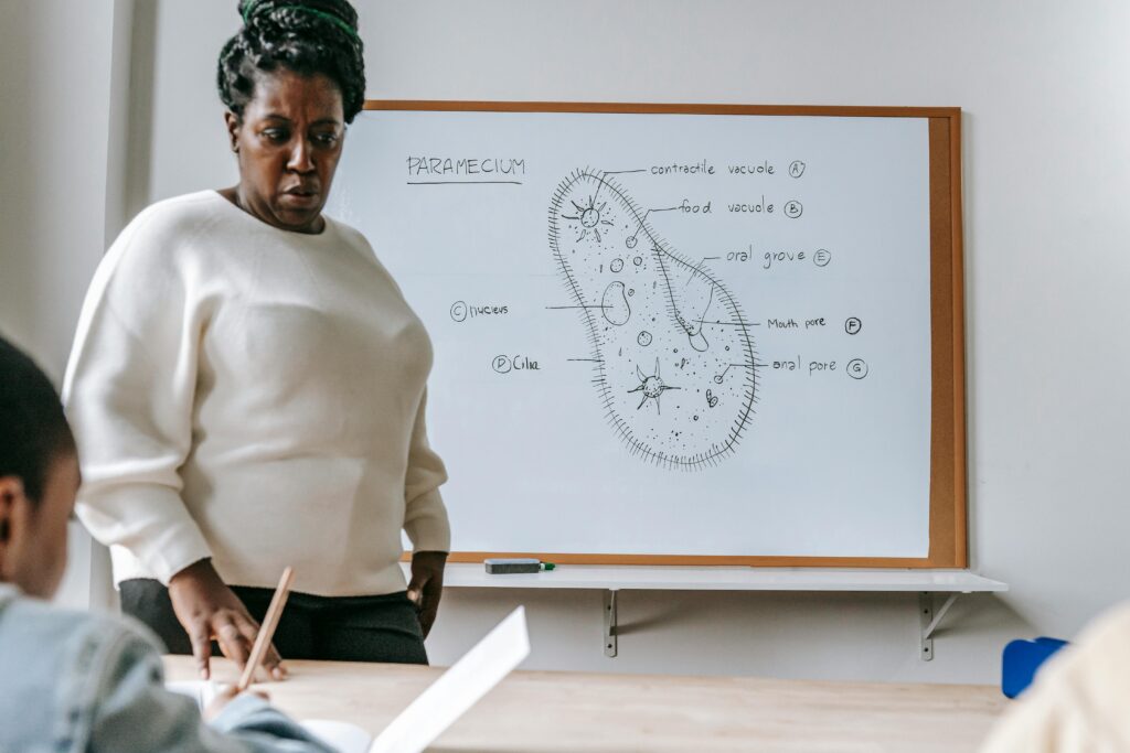 Serious African American female teacher standing near desk and explaining information during biology lesson