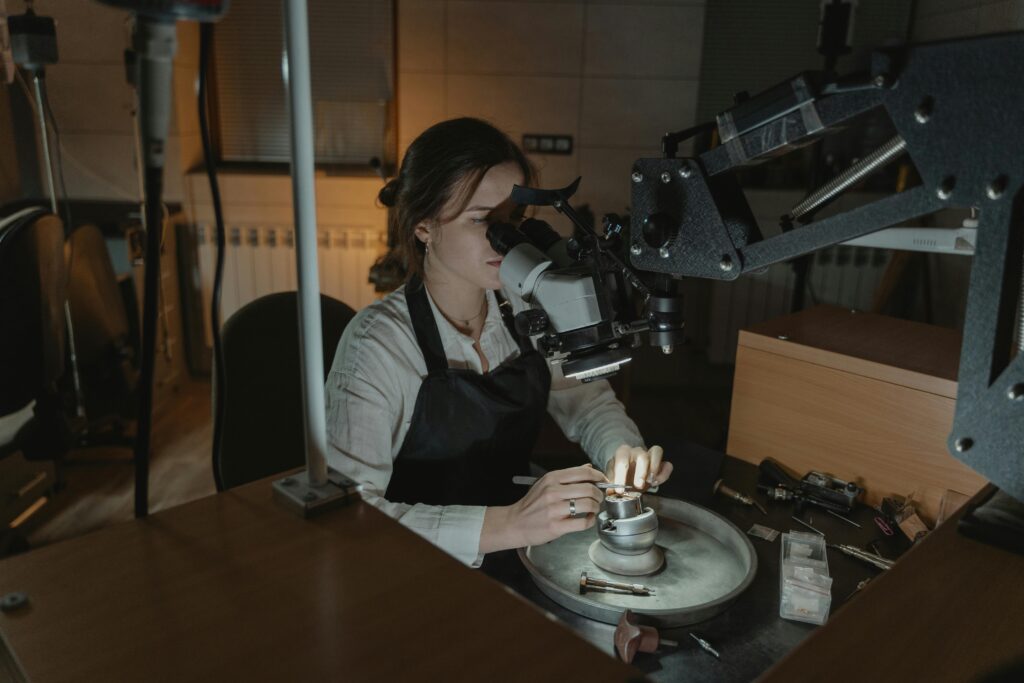 A woman jeweler crafting intricate pieces with precision under a microscope in a workshop.