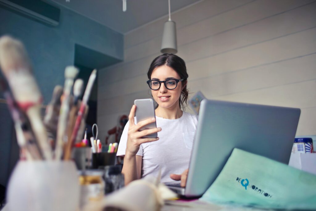 woman-in-white-t-shirt-holding-smartphone-in-front-of-laptop