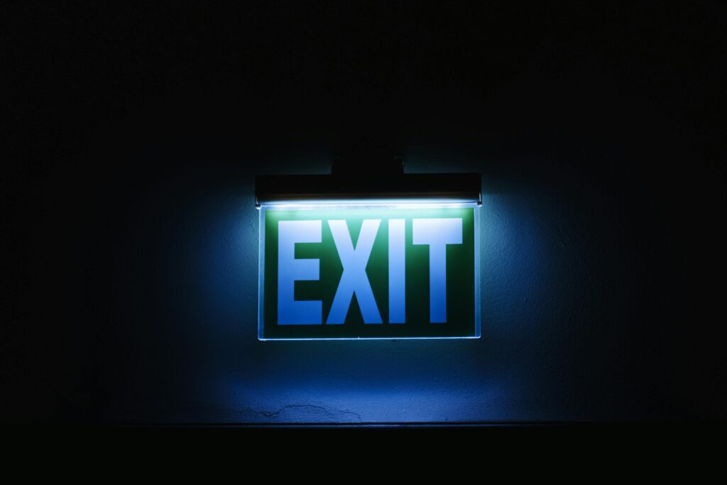 Photo of a glowing green exit sign in a dark environment, symbolizing safety and direction.