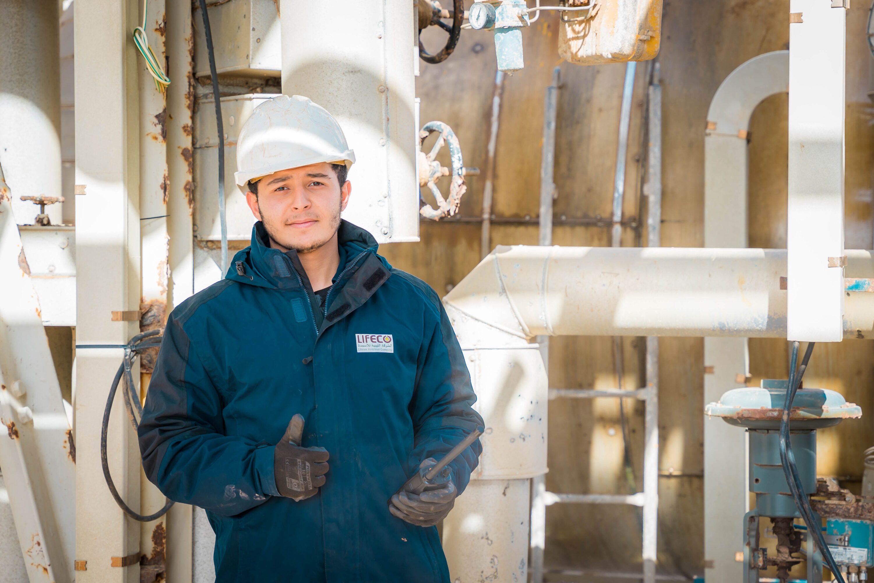 Engineer in safety gear within an industrial setting in Libya, pipes and machinery visible.