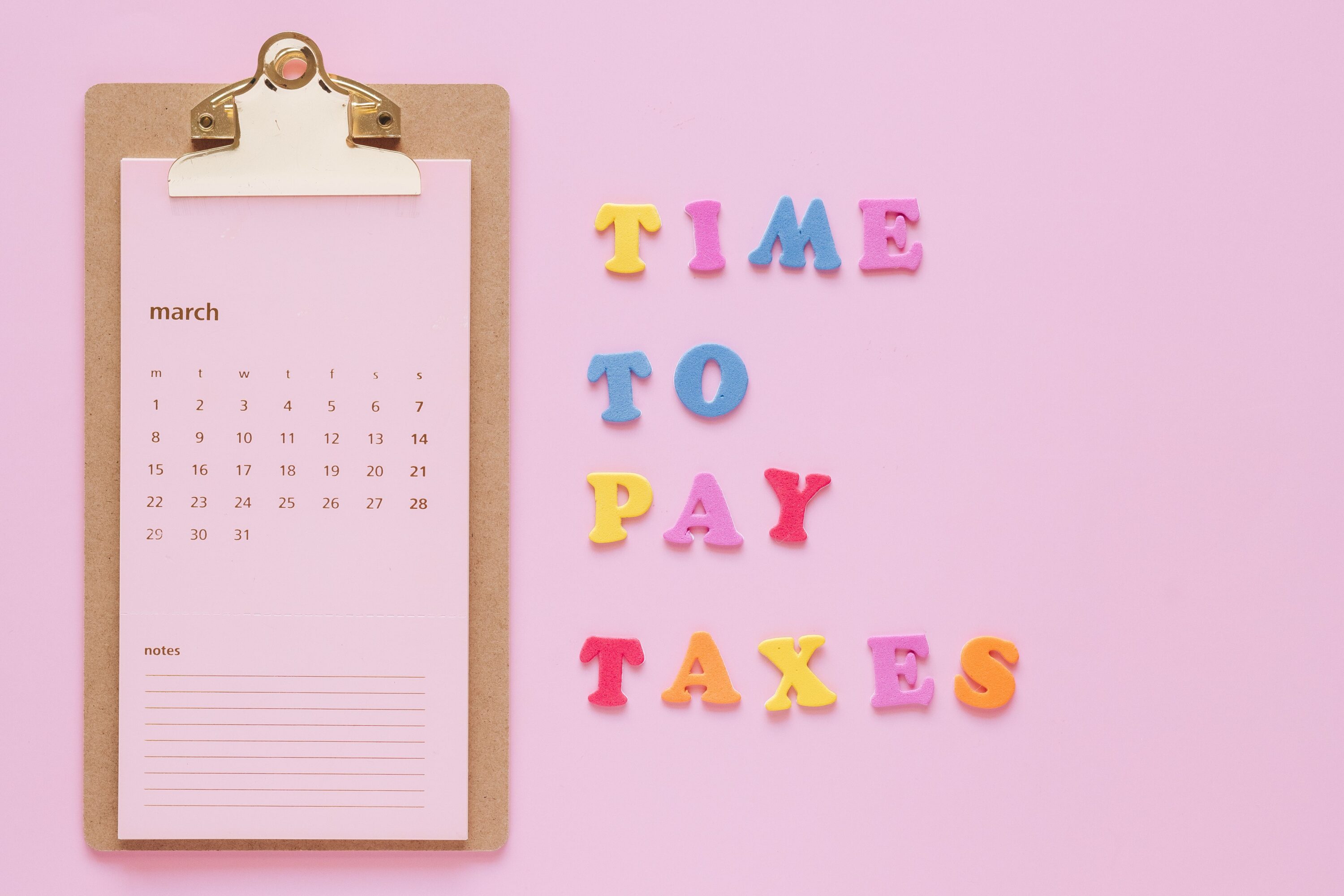Colorful tax reminder on clipboard against a pink background for March