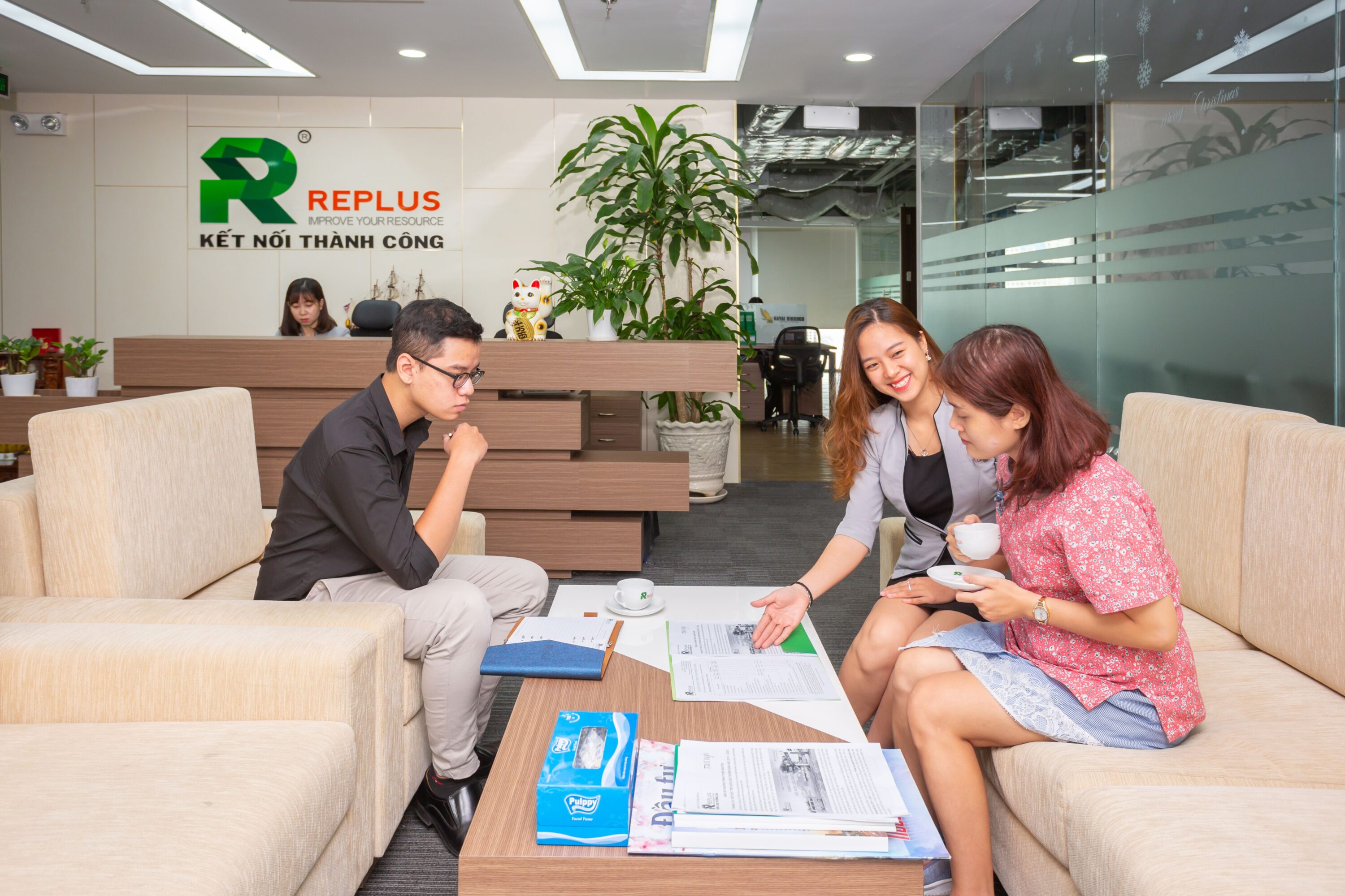 Group having a business meeting in a modern office with a receptionist in the background.
