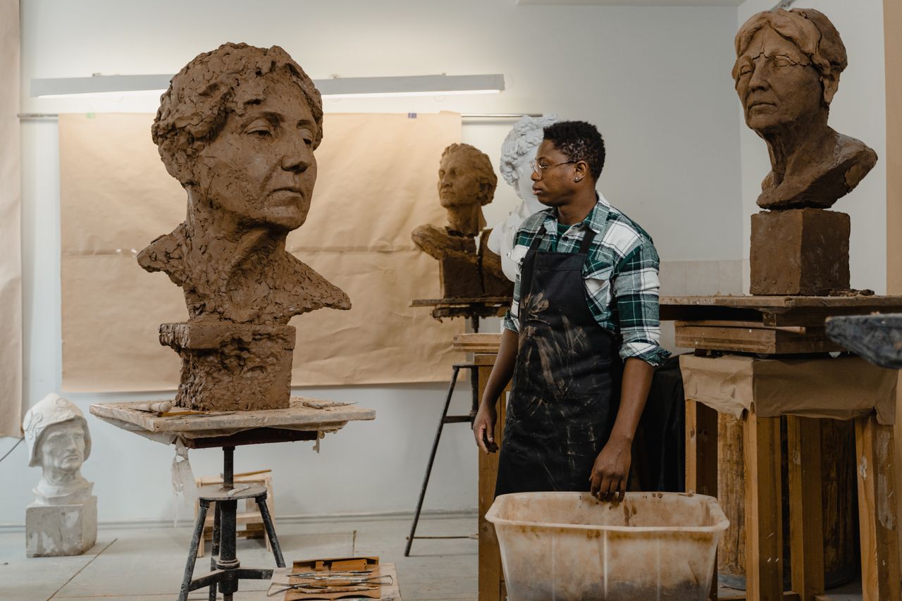 African American sculptor creating clay bust in an art studio, showcasing handmade artwork.