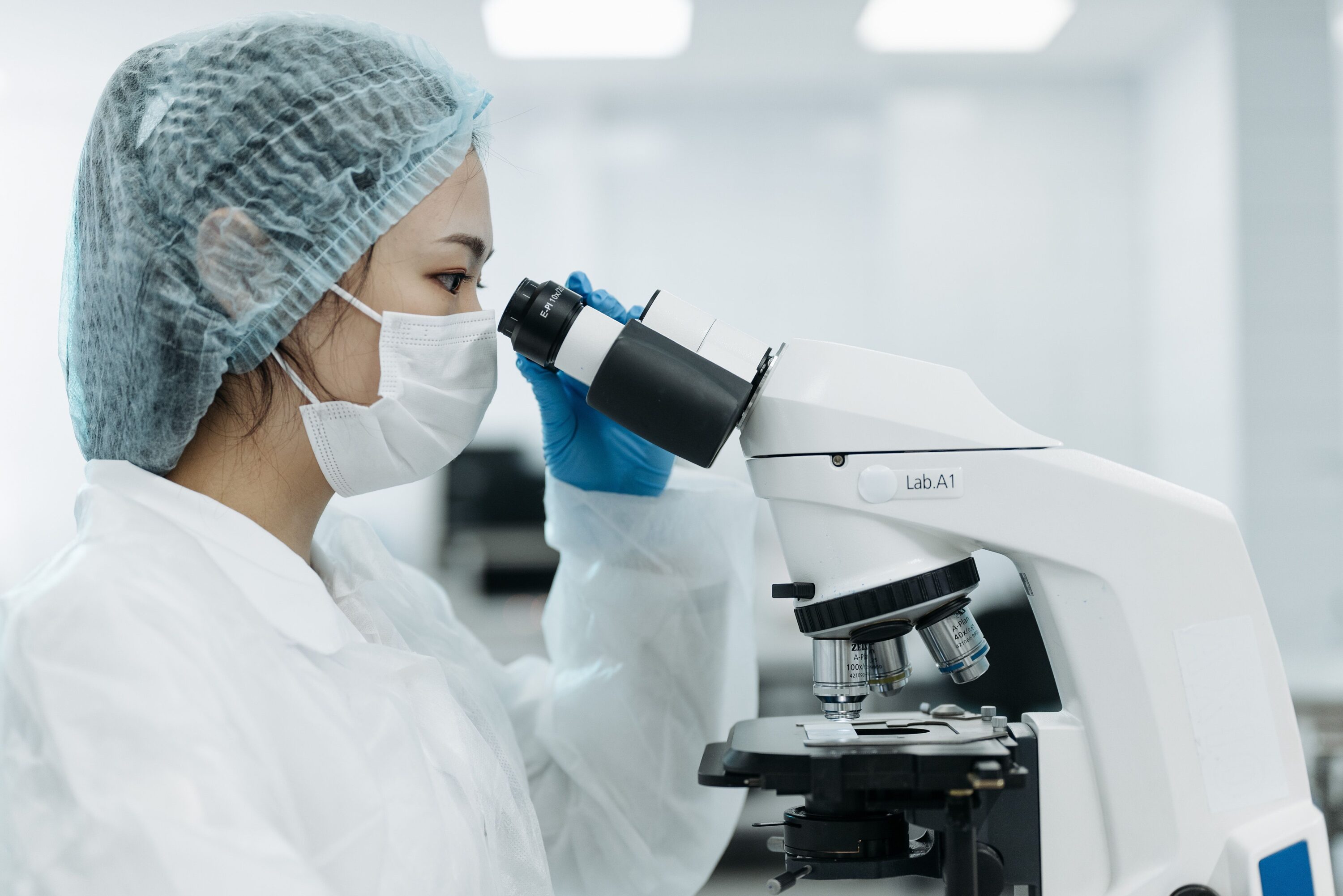 A scientist wearing protective gear uses a microscope in a laboratory setting, focusing on research.